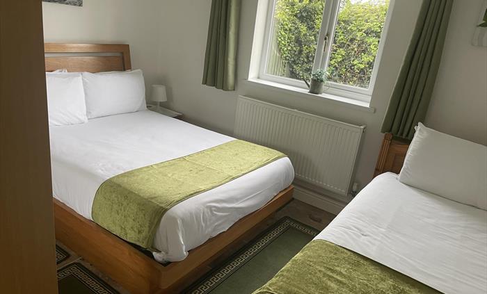Twin room showing double and single beds, window showing the view  of the private garden area.